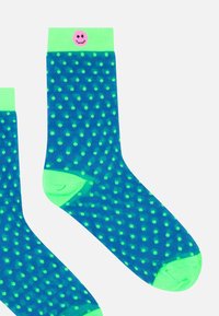 Blaue Socken mit grünen Punkten, versehen mit einem leuchtend grünen, gerippten Bündchen und einem pinkfarbenen Smiley-Detail oben.