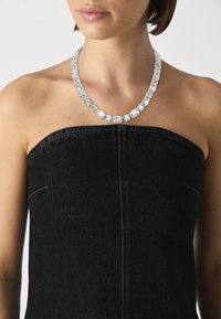 Clear crystal necklace with rectangular, faceted stones, strung on a light silver chain, worn over a black strapless top.