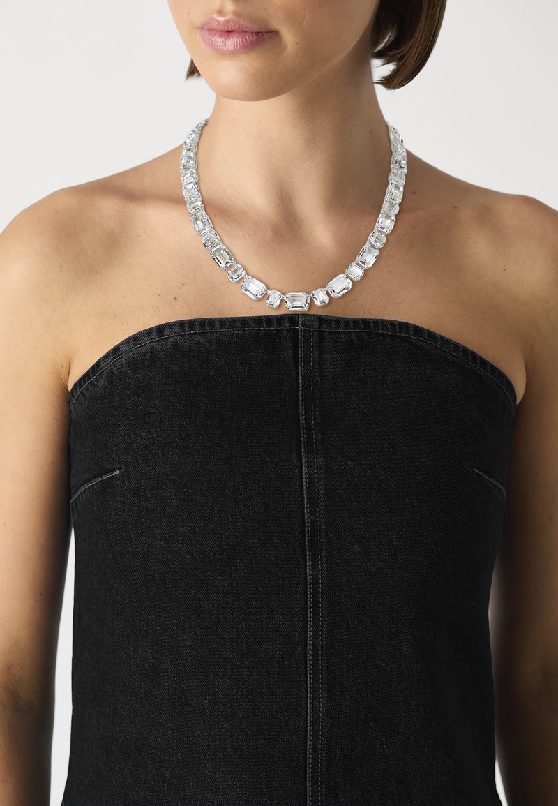 Clear crystal necklace with rectangular, faceted stones, strung on a light silver chain, worn over a black strapless top.