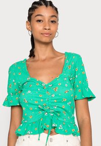 Top floral verde com mangas curtas e franzidas, decote coração, detalhes franzidos e cordão na cintura. Tecido texturizado.