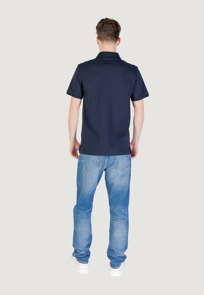 Mornarska polo majica s kratkimi rokavi, mehka tkanina in klasičen ovratnik, v kombinaciji s svetlo modrimi jeans hlačami in belimi supergami.