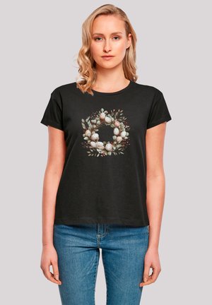 Schwarzes T-Shirt mit kurzen Ärmeln, das ein kreisförmiges Blumenkranzdesign mit gesprenkelten Eiern und grünen Blättern zeigt und aus weichem Material gefertigt ist.
