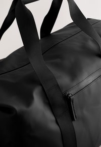 Mustast, sileda ja veekindla materjaliga duffelkott. Omab tugevaid nailonrihme ning esiküljel on lukuga tasku kauni riistvaraga.