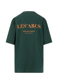 Vihreä puuvilla t-paita lyhyillä hihoilla, jossa on suuri oranssi teksti selässä: "LES'ARCS NEW BAD HABITS" ja lisäteksti alapuolella.