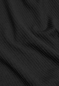Tejido negro texturizado con un sutil patrón acanalado, que ilustra un material suave y flexible que sugiere calidez y comodidad.