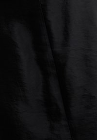 Tissu noir avec texture visible et plis créant des variations subtiles de lumière et d'ombre.