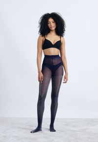 Uigenned sort bh med gennemskinnelige, teksturerede, mørke strømpebukser. Strømpebukserne har en subtil glans og en gradient fra mørkere til lysere nuancer.