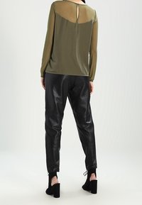Top verde oliva con maniche lunghe e dettaglio a forchetta sul retro, abbinato a joggers in pelle nera con polsini elasticizzati e texture.