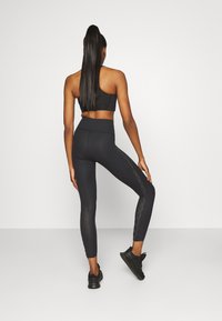 Svart sportbehå och leggings med hög midja, nätpaneler på sidorna och strukturerade mönster. Bärs med svarta sportskor.