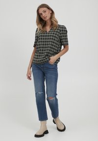 Blusa a maniche corte, con motivo scuro e scollatura a V, abbinata a jeans blu strappati e stivaletti beige chiaro con suola spessa.