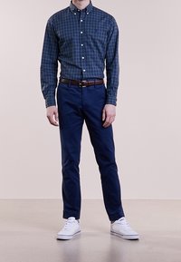 Mörkgrön och marinblå rutmönstrad skjorta med knappar, marinblå byxor, brun bälte och vita sneakers. Välbalanserad passform med klassisk krage och knapppdetaljer.