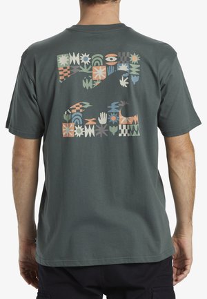 T-shirt en coton vert foncé avec un motif coloré en blocs dans le dos, comprenant diverses formes géométriques et des motifs de mains. Manches courtes, col rond.