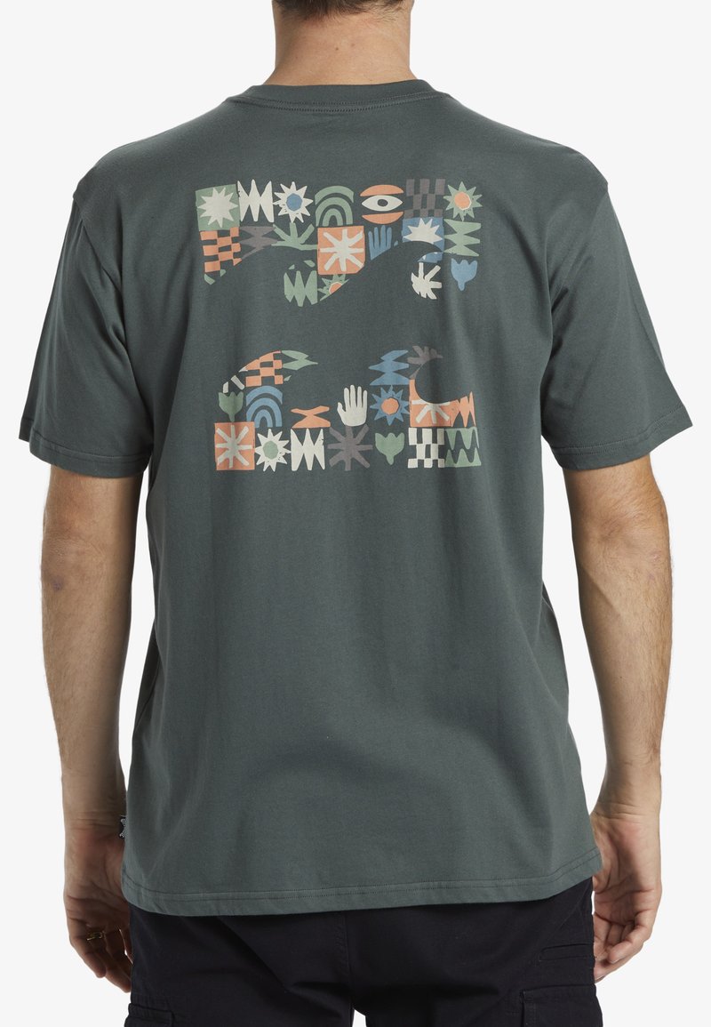 Camiseta de algodón verde oscuro con un patrón de bloques colorido en la parte posterior, con varias formas geométricas y diseños a mano. Manga corta, cuello redondo.