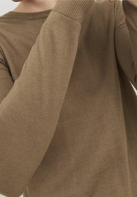 Pull marron en tricot avec un col et des poignets côtelés, présentant une texture lisse et une coupe ajustée. Vue rapprochée du tissu.