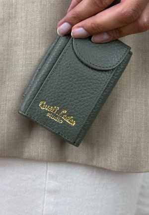 Grüner strukturierten Leder-Kartenhalter mit einer gebogenen Klappe und goldener Prägung des Textes "Quasi Leader studio." Kompaktes Design mit sichtbaren Steppdetails.