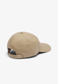 Boné bege ajustável com uma textura de algodão suave. Para-brisa curvado, orifícios de ventilação cosidos e detalhe de fecho na parte de trás.