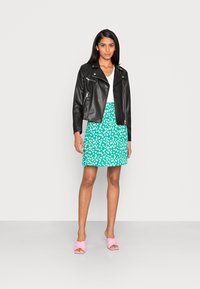 Jaspe de moto em couro preto, top branco, saia floral verde e sandálias deslizantes cor-de-rosa; um conjunto elegante e casual.