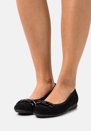 Ballerines en daim noir avec un bout arrondi, dotées d'un accent décoratif en chaîne noire à l'avant et d'une semelle en caoutchouc flexible.