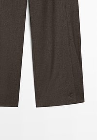 Pantalon marron foncé sur mesure avec jambes droites et un petit détail bouton près de l'ourlet sur fond blanc.