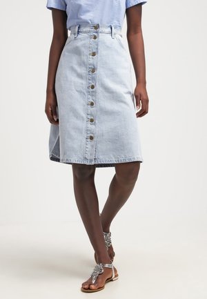 Hellblauer Jeansrock mit tailliertem Bund, A-Linien-Form, vorderer Knopfverschluss und seitlichen Taschen. Begleitet von verzierten Sandalen.