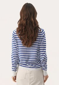 Sweter w paski w kolorze niebiesko-białym, wykonany na drutach, z długimi rękawami, ściągaczami na mankietach i luźnym krojem. Miękka tekstura, widoczne detale szwów na dole.