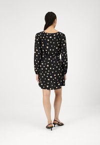 Μαύρο φόρεμα με μακριά μανίκια, με μπεζ τετράγωνο σχέδιο. Το ύφασμα φαίνεται ελαφρύ, με δέσιμο στη μέση και φαρδιά ποδιά.