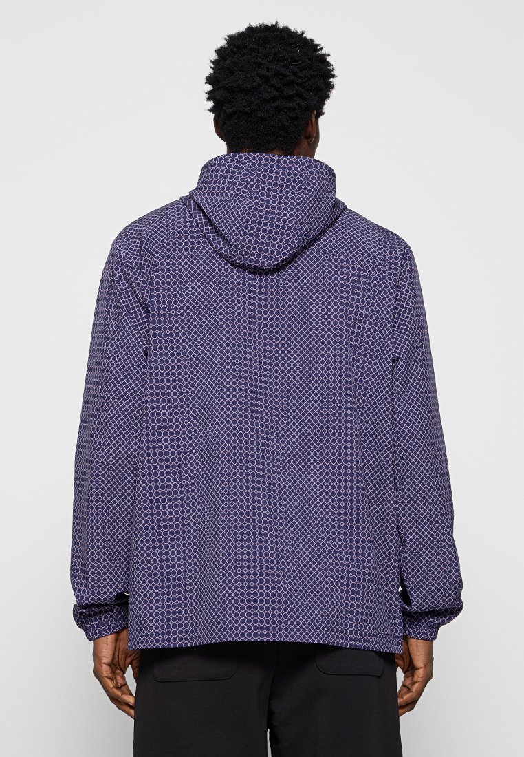 Giacca a cappuccio viola con un motivo geometrico, dotata di polsini elasticizzati e una vestibilità rilassata. Il tessuto leggero offre comfort e flessibilità.
