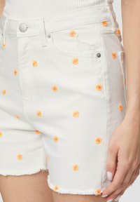 Białe szorty dżinsowe z pomarańczowym i różowym haftem kwiatowym, z postrzępionym dołem i standardowymi kieszeniami. Zapięcie na metalowy guzik w pasie.