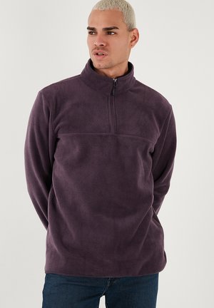 Purple fleece pullover with a half-zip collar, relaxed fit, featuring a horizontal seam across the chest, smooth texture, and long sleeves.