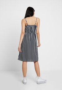 Randig midiklänning med tunna axelband, marinblå och cremefärgade vertikala ränder, figurnära överdel och utsvängd kjol, kombinerad med vita sneakers.