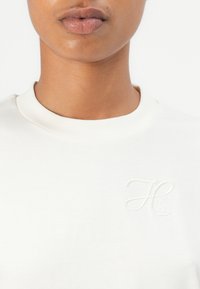 White sweatshirt with a crew neck and an embossed logo "HUGO" on the left side. Smooth fabric texture, minimalistic design.