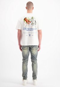 Witte katoen T-shirt met een grafische print van zeevruchten en tekst op de rug. Gepaard met vervaagde blauwe jeans en witte sneakers.