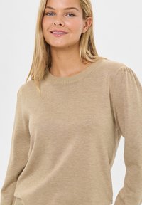 Bežani džemper od pletenine s rebrastim okovratnikom, dugim napućenim rukavima i finom teksturom. Jednostavan dizajn, bez uzoraka ili akcenta.