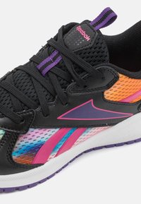 Chaussure de sport noire avec des panneaux en maille, des accents en dégradé multicolores, des détails violets et roses, et une semelle blanche avec une semelle extérieure violette.