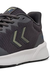 Mörkgrå träningssko med ovandel i mesh, reflexdetaljer och en dämpad vit sula. Har logotyp och sicksackmönster på sidan.