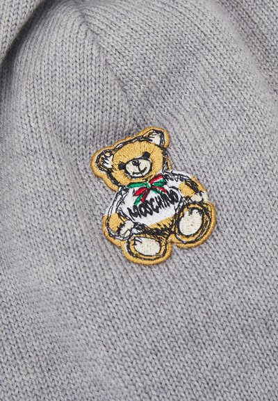 Hallide kootud kangas, millel on kollase äärisega tikitud karupoeg, kes kannab valget särki, millel on must kiri "Moschino".