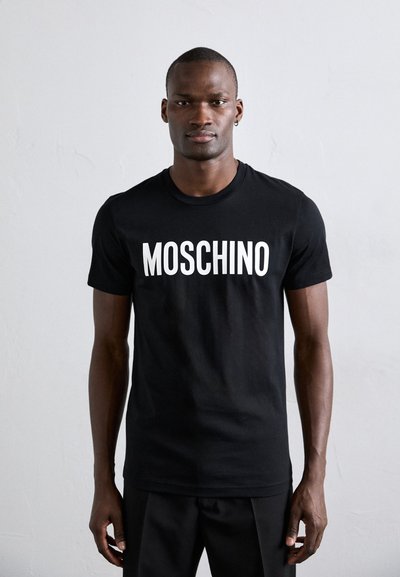 Fekete pamut póló, amelyen vastag fehér betűkkel szerepel a "MOSCHINO" felirat a mellkason. Normál szabású, kerek nyakkivágással és rövid ujjakkal.