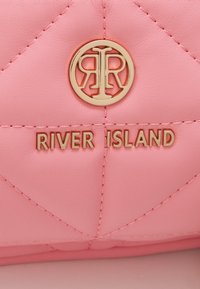 Pink quilted faux leather bag featuring a gold-tone circular logo and "RIVER ISLAND" embossed in gold text.