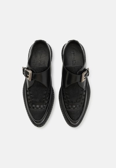 Chaussures noires avec un dessus en cuir lisse, des détails tissés, un panneau texturé et une boucle métallique. Comprend une semelle intérieure rembourrée et une semelle en caoutchouc.
