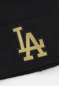 Gorro negro con un diseño de punto texturizado. Presenta un destacado logo dorado "LA", contorneado en negro, cerca del borde inferior.