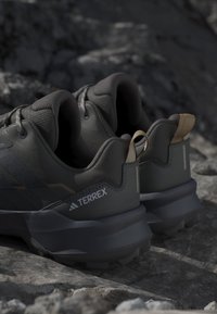 Zapatillas de senderismo Terrex gris oscuro con suelas texturizadas descansando sobre terreno rocoso.