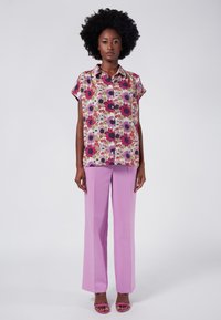 Blusa floreale a maniche corte con motivi rosa, viola e bianchi, abbinata a pantaloni larghi lavanda e sandali rosa coordinati.