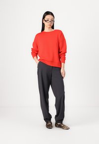 Red sweatshirt with a relaxed fit and crew neckline, paired with dark gray tapered pants and leopard print flats. Simple, modern design.
