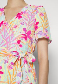 Vestido envelope floral em tecido multicolorido com fundo azul claro, apresentando padrões vibrantes em rosa, laranja e verde, e um detalhe de cintura atada.