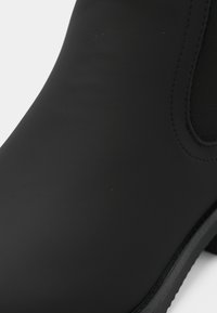 Boots negre impermeabile până la glezne, cu un finisaj neted, mat, panouri laterale elastice și o talpă robustă din cauciuc. Vârf rotund și fără modele vizibile.