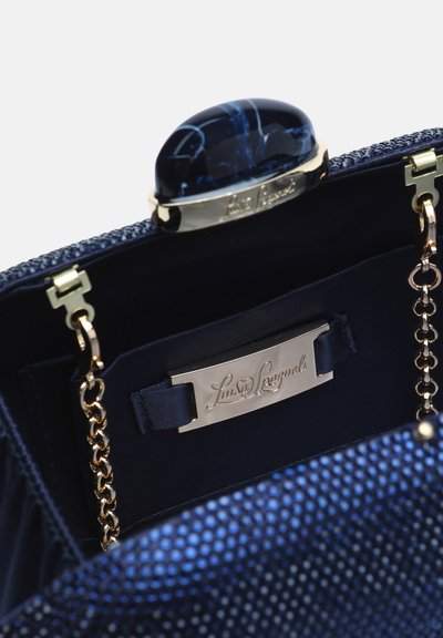 Pochette bleu foncé ouverte avec extérieur texturé, bandoulière chaîne dorée et fermoir en pierre bleue polie, montrant la plaque de marque intérieure avec logo gravé.