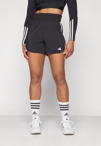 Pantalones cortos deportivos negros con una amplia cinturilla elástica, que presentan franjas laterales blancas y un pequeño logotipo. Combinados con calcetines blancos con rayas negras.