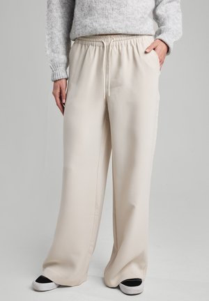 Beige wide-leg pants with an elastic waistband and drawstring; smooth fabric with side pockets; paired with black and white sneakers.