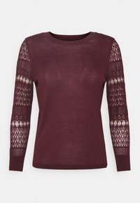 Langärmliger, weinroter Strickpullover mit Rundhalsausschnitt, ausgestattet mit halbtransparenten Ärmeln in Spitzenmuster und einem einfarbigen Körper.