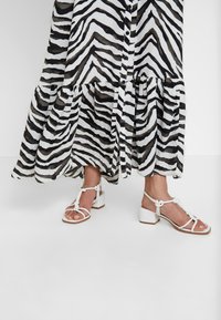 Zebramönstrad, svart och vit, flödande klänning med en volangkant; matchad med vita sandaler med remmar och klack.